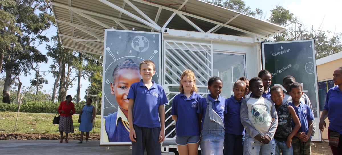 A group of children stand in front of a Solar Learning Lab