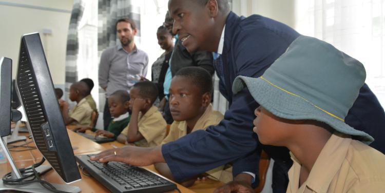 A group of students using a computer with guidance from a teacher
